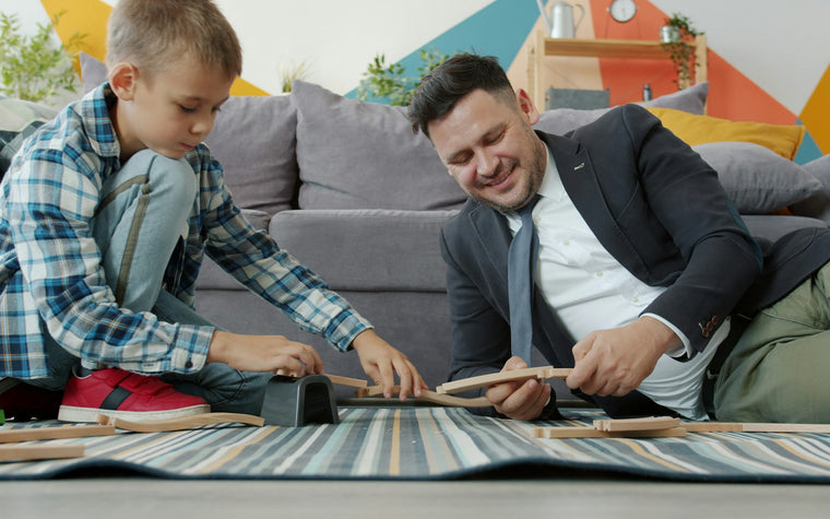 Tētis un mazs dēls mājās kopā rotaļājas ar rotaļu vilcienu